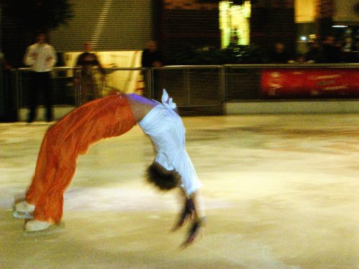 A skater performing a backbend on ice in orange pants.